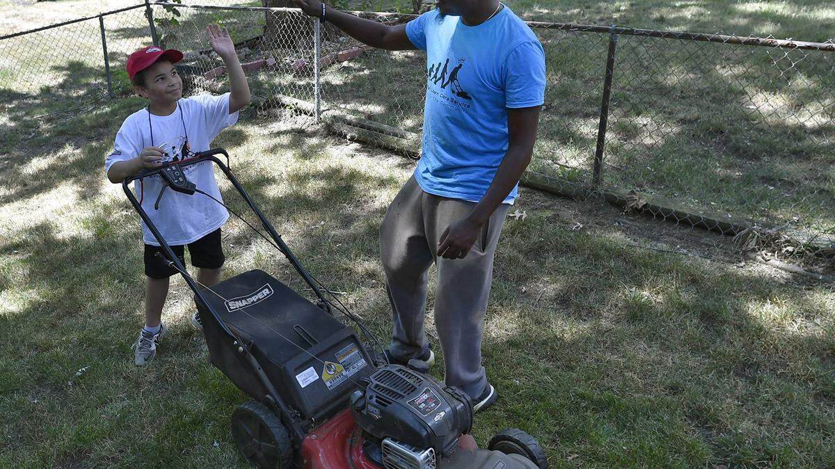 Rodney Smith, right, of Huntsville, Ala., gives a high five to Erron Blockmon, 9, of Lee's Summit, Kan., after they finished mowing a lawn Tuesday afternoon, July 10, 2018 in Overland Park, Kan. Smith aims to help mow lawns for elderly, veterans or single moms in all 50 states. He calls his effort, "Making a difference one lawn at a time." Smith has only four more states to go after his stop in Kansas.