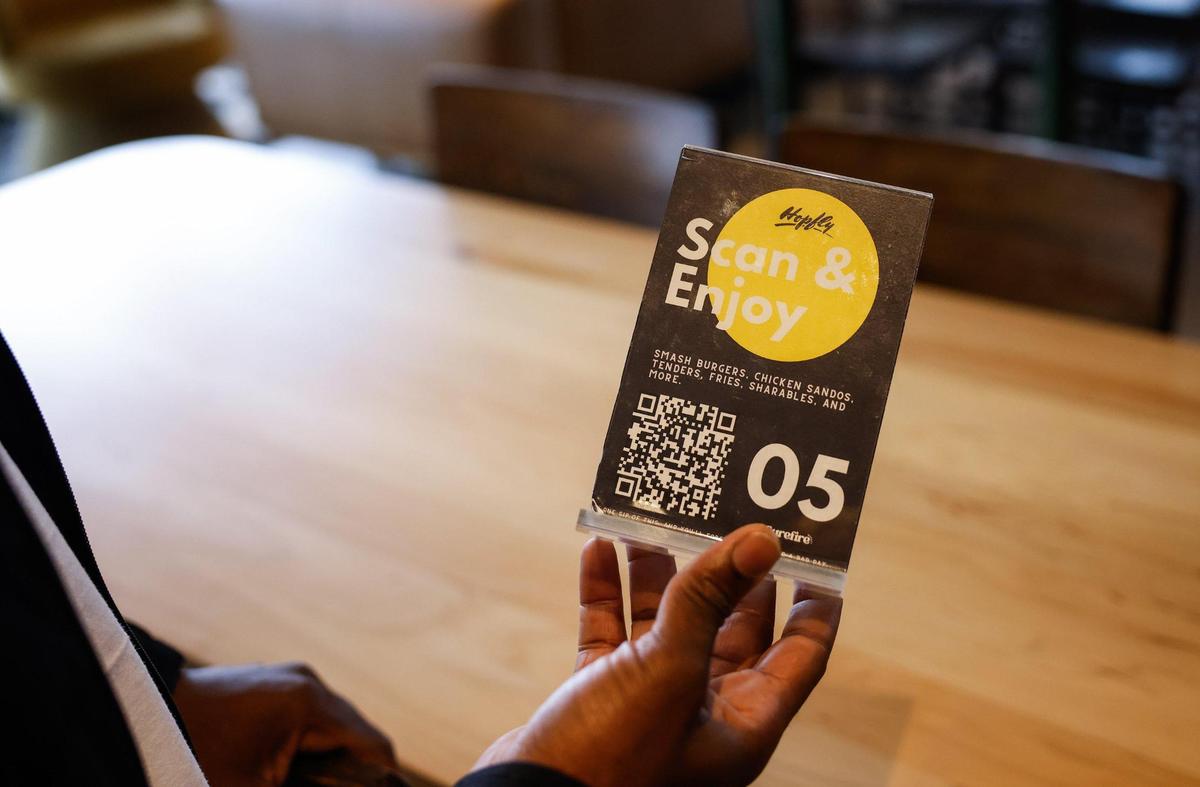 Magloire Lubika, holds one of the QRC code menus for their food truck, Surefire, located at each table inside Hopfly Brewing Company on Mint Street in Charlotte, NC on February 20, 2025. The scannable menus make it easier for brewery patrons to place orders and wait inside instead of waiting in a long line.