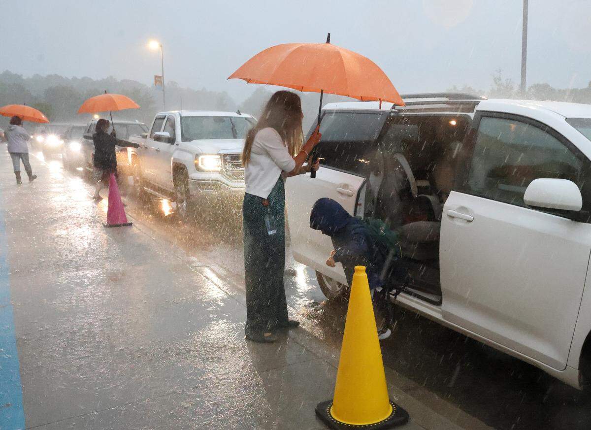 School staff at Fort Mill’s River Trail Elementary School try to stay dry as they help kids out of cars on the first day of school. The district held school despite Tropical Storm Debby soaking the area.