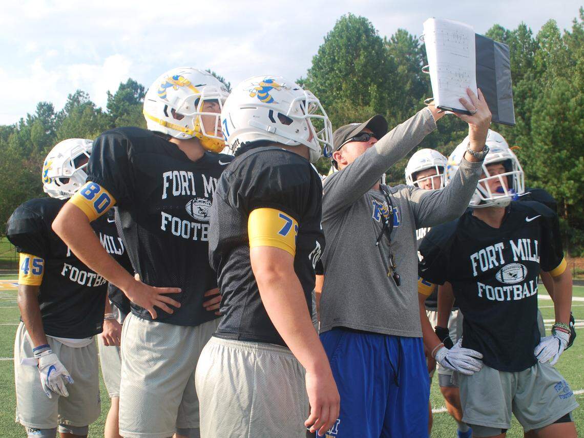 Fort Mill head football coach Rob McNeely, lifts his binder and reviews a defensive play with his team during practice.