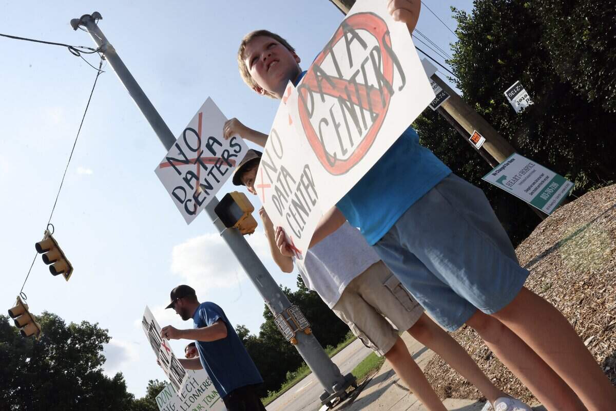 Leo Barnette, 10, holds “no data center” signs, along with his cousin A.J. Barnette, center, and his dad, Alec Barnette, on  Saturday, July 18, 2026, outside the Chester, South Carolina Walmart Supercenter.