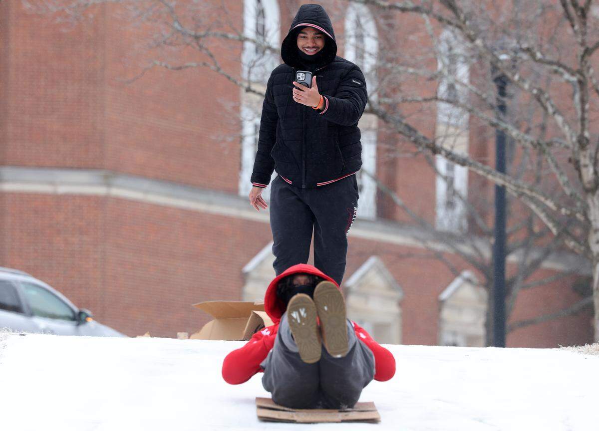 Eric McClain slides down a hill on a cardboard box Sunday, Jan. 25, 2026 at Winthrop University in Rock Hill, S.C. as Anthony Gray records.