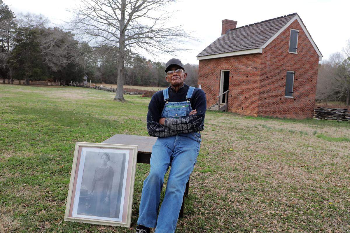84-year-old Wali Cathcart’s great-grandmother Lila was enslaved at Historic Brattonsville. Cathcart is shown here with a photo of his grandmother Fannie, who was born shortly after the slaves were freed.