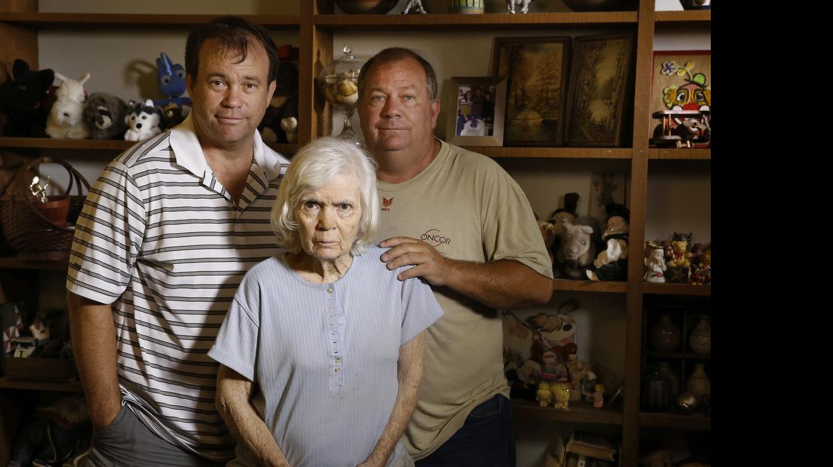 
Kent, left, and Mark Olds stand with their mother Gail, 80, in her Dallas home. Gail has dementia but denies it. Her sons have to pay her bills and help her with some of her daily tasks. 
