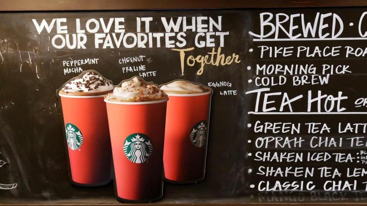 Red paper cups are featured on a chalkboard menu behind the counter at a Starbucks coffee shop. It’s as red as Santa’s suit, a poinsettia blossom or a loud Christmas sweater. Yet Starbucks’ minimalist new holiday coffee cup has set off complaints that the chain is making war on Christmas.