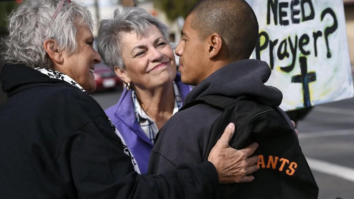 Ivan Mendoza, who was riding his bike when he stopped for a prayer, listens as Virginia La Salle, left, and Linda Crowder, center, chat with him at a pair of canopies set up for free prayers on Friday.