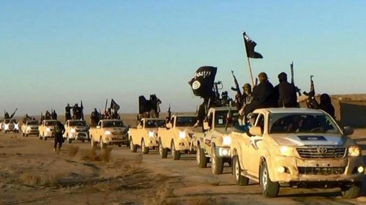 In this undated file photo released online in the summer of 2014 on a militant social media account, which has been verified and is consistent with other AP reporting, militants of the Islamic State group hold up their weapons and wave its flags on their vehicles in a convoy on a road leading to Iraq, in Raqqa, Syria. The extremist group that once bragged about minting its own currency is now accepting only U.S. dollars in Raqqa, slashing salaries across the board and imposing “exit fees” for those trying to leave its domain.