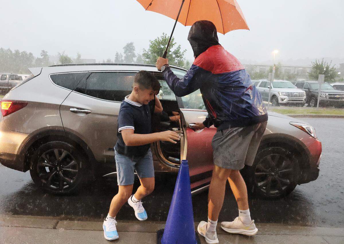 A boy gets out of a car in the drop-off line at River Trail Elementary School Thusday as a school worker helps. Fort Mill and Rock Hill schools opened the doors for the first day of school despite hurricane Debby soaking the area.