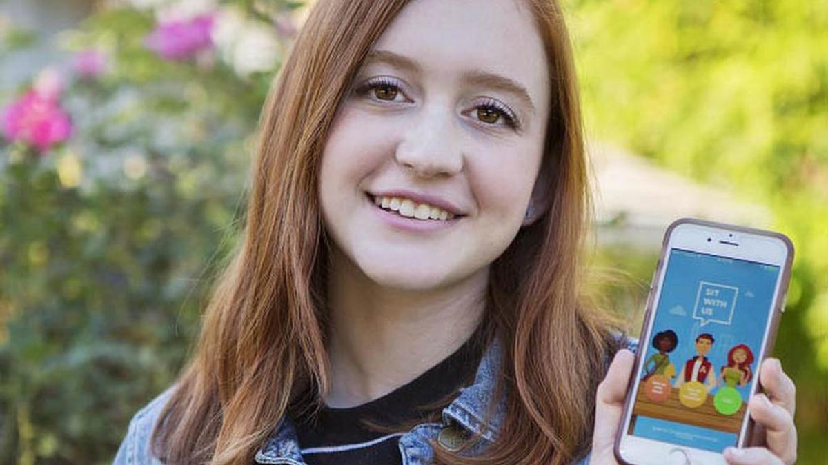 Natalie Hampton holds her phone showing her “Sit With Us” app.