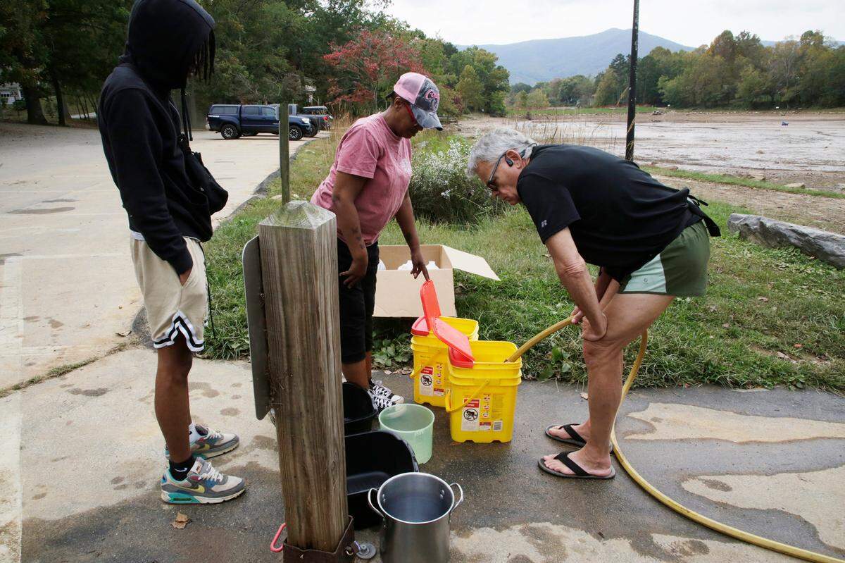 Lashonda Lytle, center, Robert Wharton, right, fill buckets with water Friday, Oct. 4, 2024 in Black Mountain, N.C.