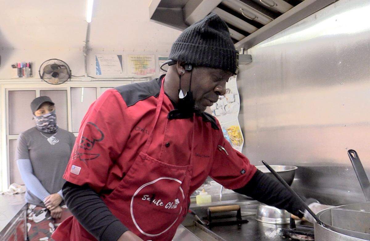 Tyrone Jenkins makes a burger on his food truck, Salute Chew, as his wife Ceslie Jenkins waits for customers.