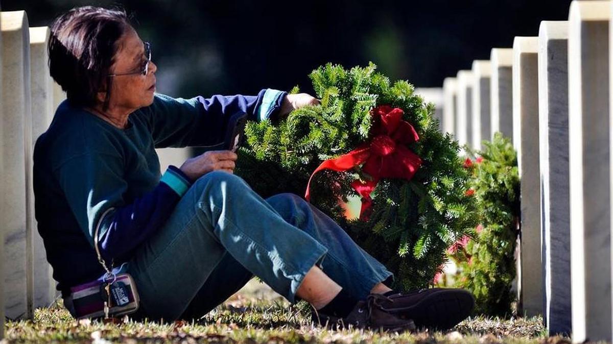 Tess Reusch, of Beaufort, rests against a gravestone as she places a wreath on her husbands grave during the Wreaths Across America Day event at the Beaufort National Cemetery on December 13, 2014.