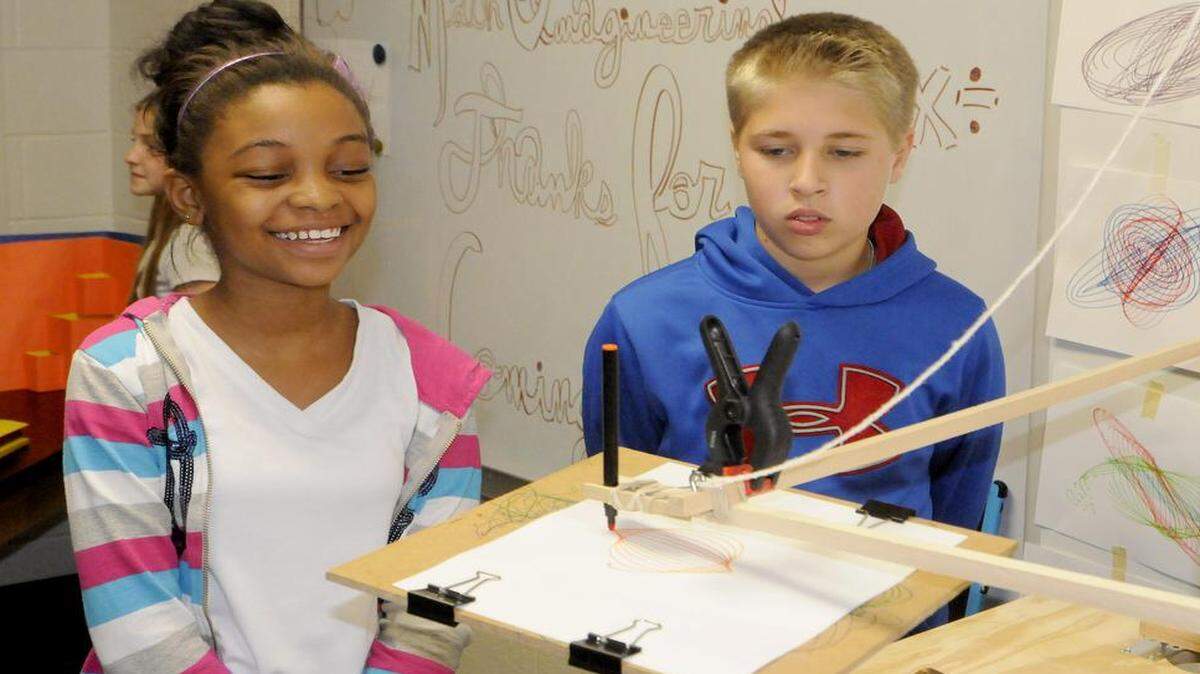 
Jamyra Collins, left, and Trip Scoggins observe the use of a harmonograph, a mechanical apparatus that employs pendulums to create a geometric image. Students talked about the factors that affect the image.
