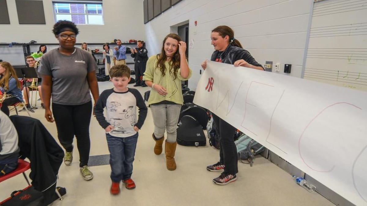 Nation Ford High Marching Band members Amaya Britton (left) and and Maggie Hays (right) escort Cooper Haynes, 7, past a "Welcome Cooper" to the front of the band room to be introduced to the rest of the band. Cooper and his family came to thank Amaya and Maggie for returning his prized wallet after they found it on charter bus during a recent band trip. Cooper had been on the same bus a few days earlier for a school trip and lost the wallet.