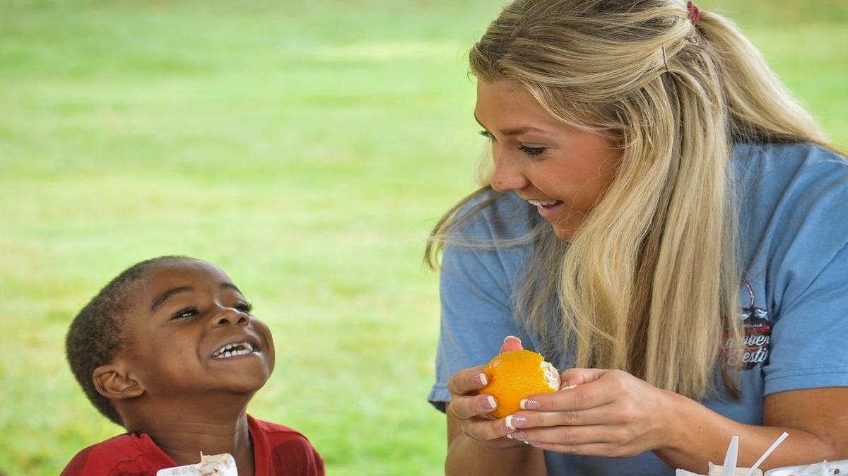 2015 Teen S.C. Strawberry Festival Queen Casey Hillman shares a laugh and an orange with one of the kids at Steele Street Park in Fort Mill. Strawberry Festival Queen volunteered to help with last week’s York County Summer Feeding program.