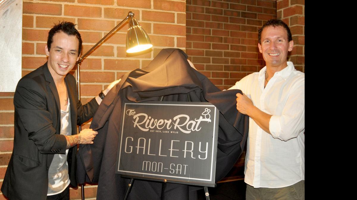 
Artist Jonay di Ragno, left, and Gerry Woods, event planner at The River Rat, unveil the Art Gallery sign for the Lake Wylie restaurant during Art Night July 22. 
