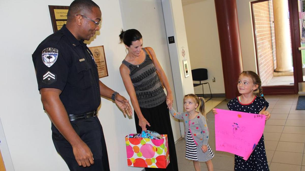 Lila and Emma Miller, with their mom, Julie Miller, present Fort Mill Police Dept. Crime Prevention Specialist Johnathan Gilbert with a poster and goodie bag filled with candy and other treats for FMPD officers. The girls wanted to present the gifts to thank the officers for the service to the town.