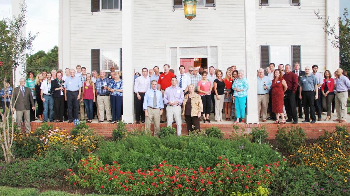 
Members of Montcross Area Chamber of Commerce stand on the porch of the historic 1850 John McLean house, which will be the McLean sales center at 175 Armstrong Road in Belmont, during a network after hours event. 
