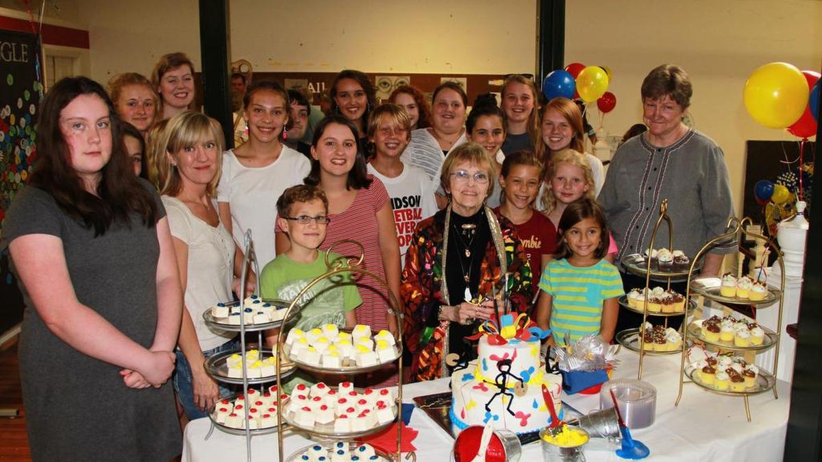 
Jeaniene Dibble prepares to cut the cake surrounded by students and other teachers at Art by J in Belmont. 
