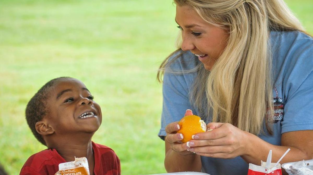 
2015 Teen S.C. Strawberry Festival Queen Casey Hillman shares a laugh and an orange with one of the kids at Steele Street Park in Fort Mill. Strawberry Festival Queen volunteered to help with last week’s York County Summer Feeding program. 
