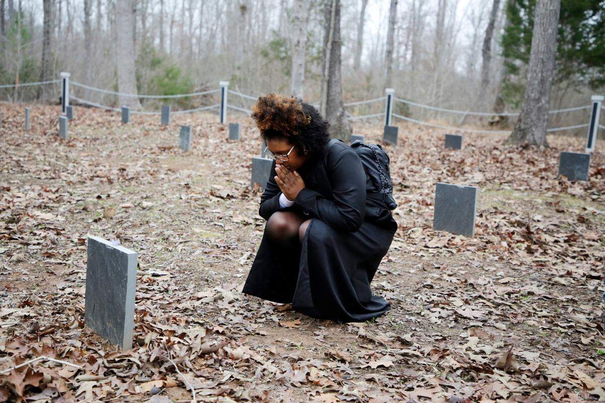 Jada Rosby prays at a gravesite Saturday where an enslaved person lays to rest on the property of Andrew Lazenby. Lazenby has restored the cemetery where enslaved people were buried.