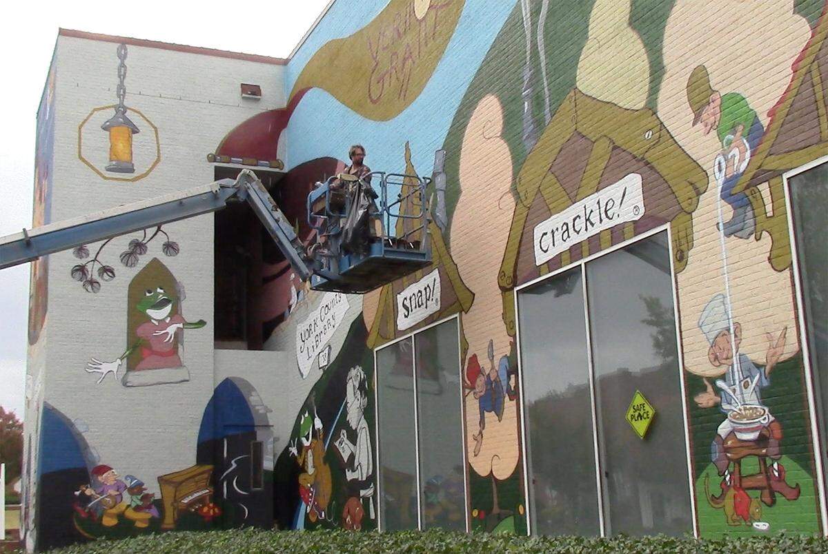 Charlotte-based muralist Osiris Rain works on a mural depicting the artwork of Vernon Grant on the side of York County Library in Rock Hill, S.C.