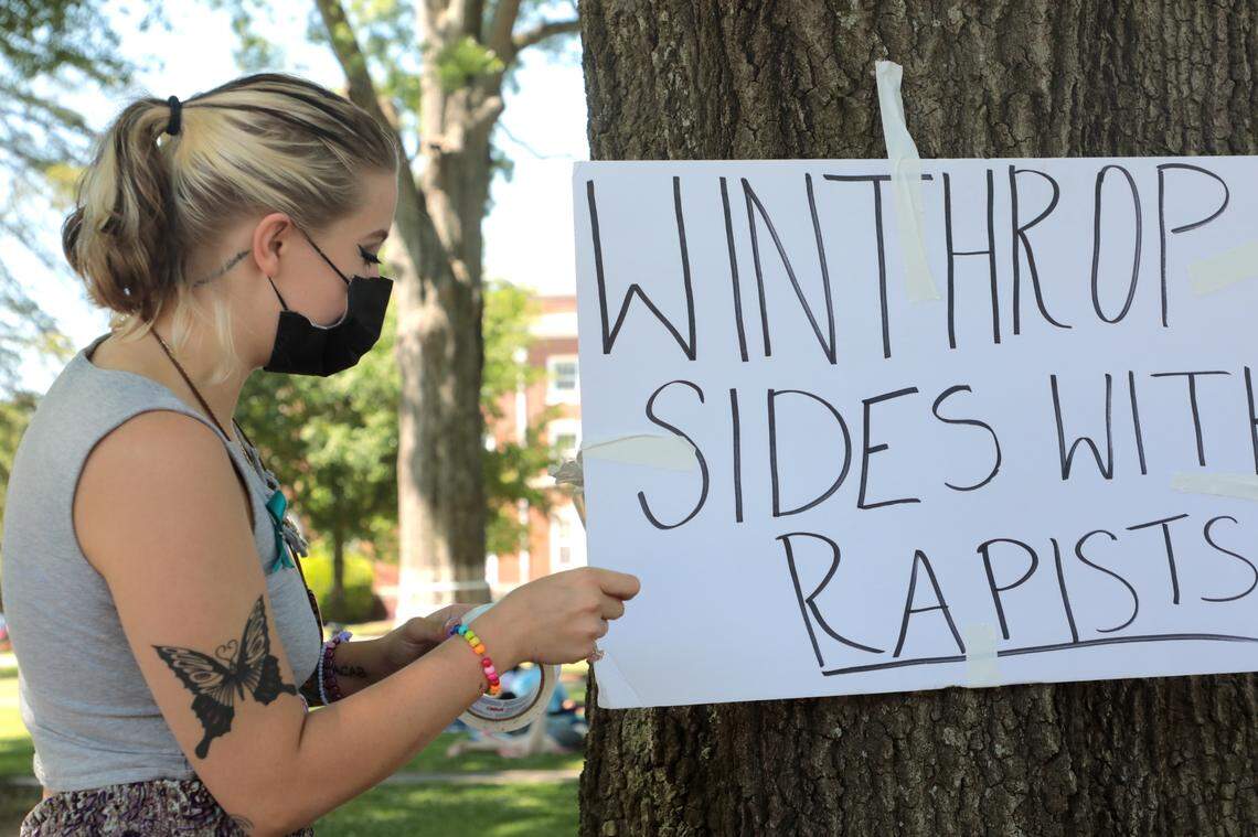 Winthrop University student Grayce Kellam tapes a sign to a tree Wednesday.