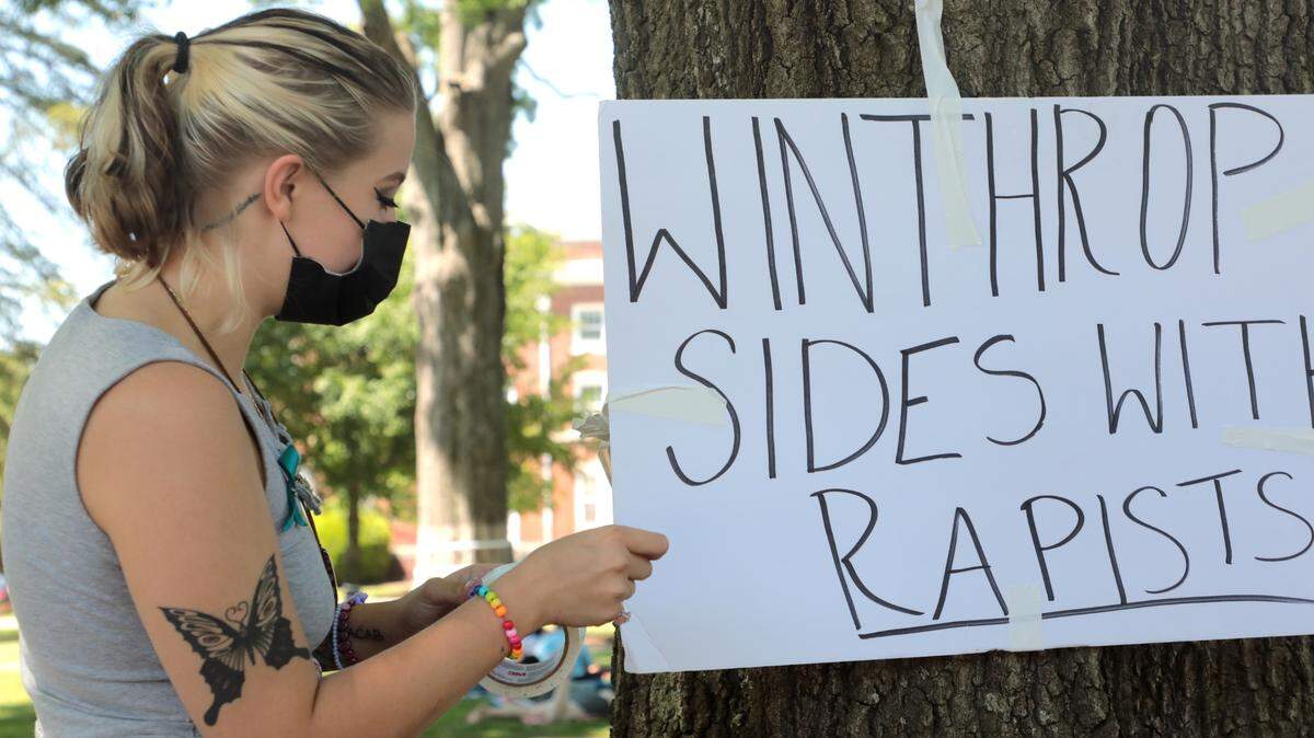 A Winthrop University student tapes a sign to a tree in 2021 as part of a protest against sexual assaults, and the way they’re handled, on Winthrop’s campus.
