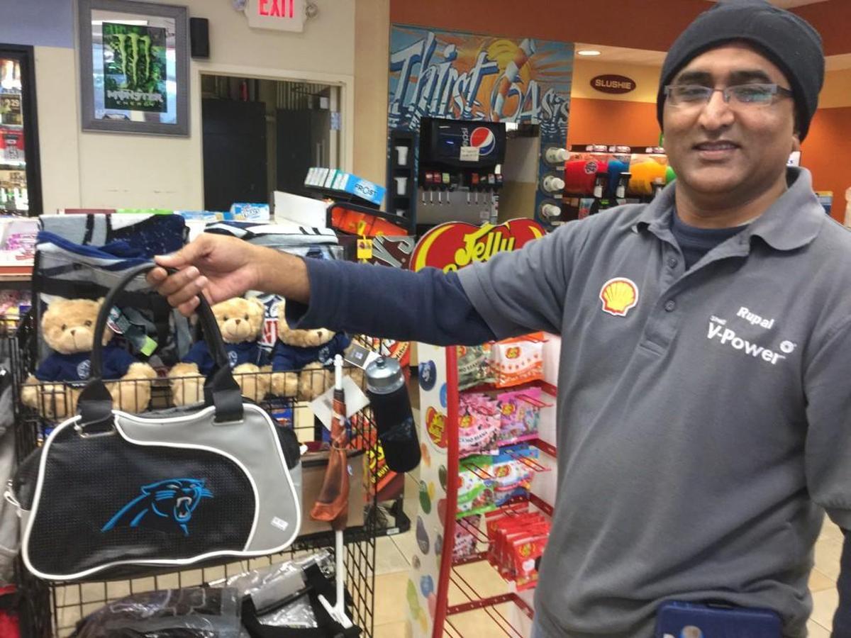 Rupal Patel, an immigrant from India and Carolina Panthers superfan for 20 years, shows off one of the bags he sells at his Rock Hill store.