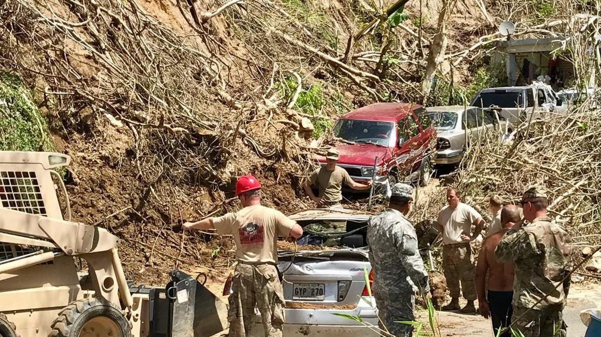 U.S National Guard Soldiers with the 122nd Engineer Battalion, S.C. Army National Guard and 190th Engineers, Puerto Rico Army National Guard, work together to dig out an automobile with a skid-loader that had been buried in debris blocking the road to a family home since Hurricane Maria impacted the island.