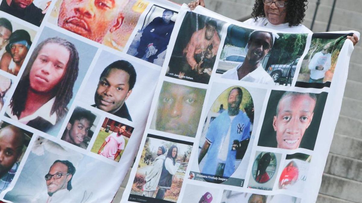 Tyese Miller holds banners with photographs of victims of gun violence during a Statehouse rally Wednesday to increase waiting periods for hand guns.