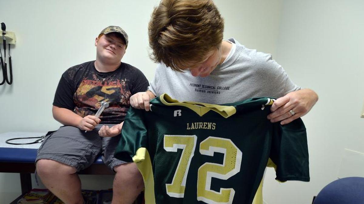 
 Kimberley Lovejoy holds up the football uniform of son Jacob Lovejoy, a 16-year-old stroke survivor, progress during a recent checkup.
