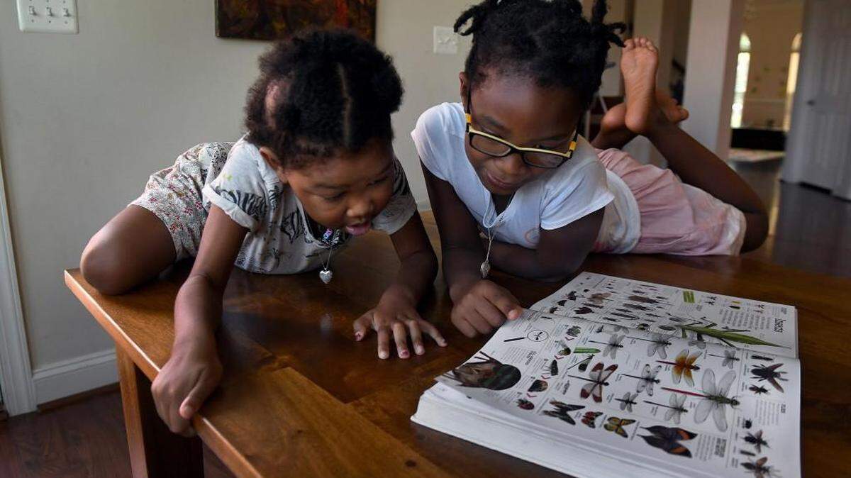 Eden and her sister Sade, 7, look at a picture book of animals and insects as they play in their home in Bowie, Maryland.