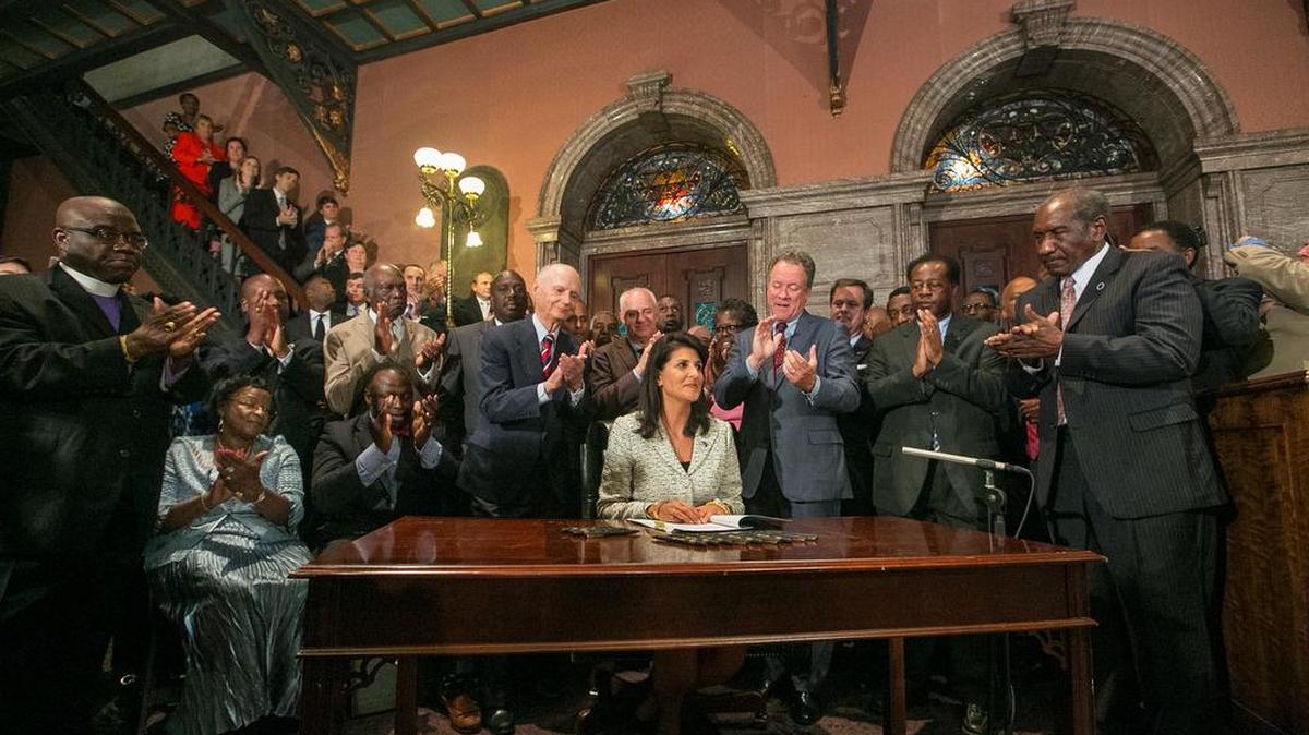 
Gov. Nikki Haley, surrounded by former governors and relatives of victims from the Charleston church shooting, signs the bill to remove the Confederate flag from the State House grounds in July.
