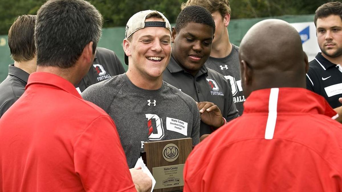 Davidson senior linebacker Nate Casey, center, celebrates with his head coach Paul Nichols, left, and safeties coach Justin Hood, right, after receiving his 2016 Allstate AFCA Good Works Team trophy on Sept. 15.