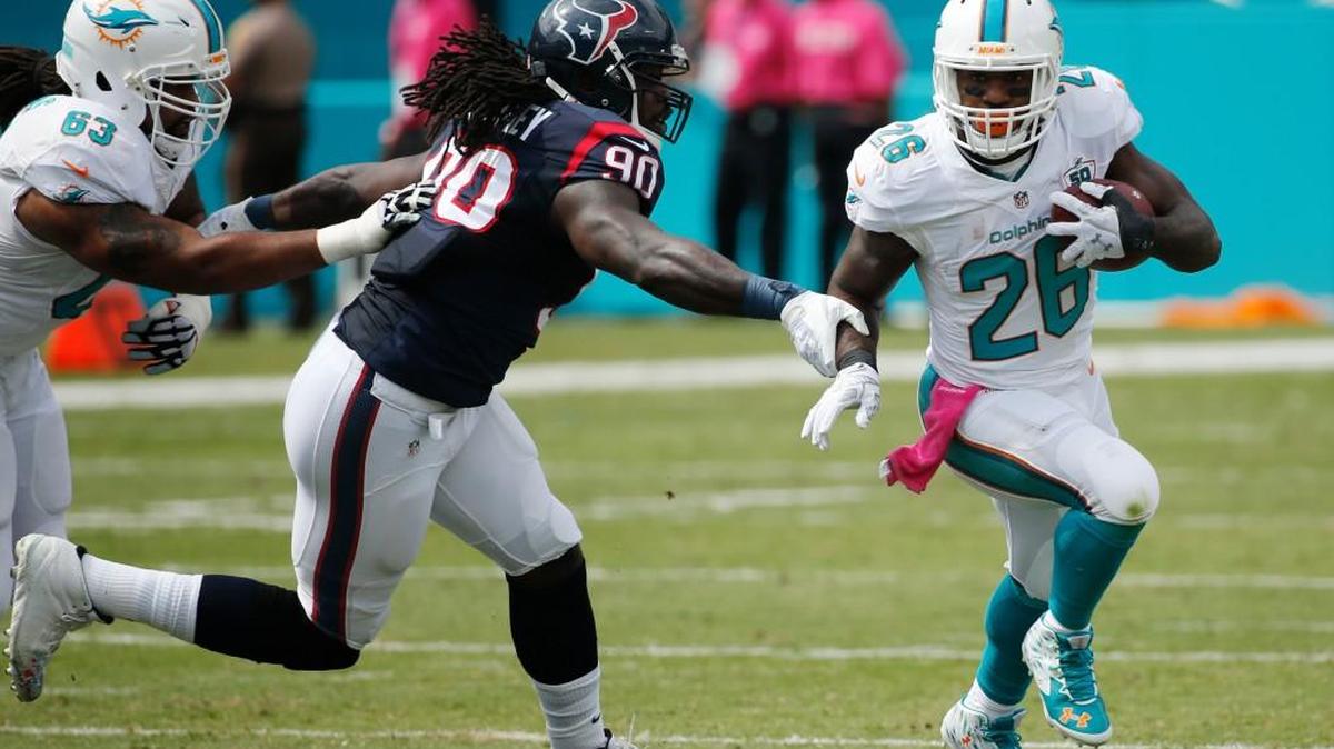 Miami Dolphins running back Lamar Miller (26) avoids a tackle by Houston Texans outside linebacker Jadeveon Clowney (90) during the first half of an NFL football game, Sunday, Oct. 25, 2015 in Miami Gardens, Fla. To the left is Miami Dolphins offensive guard Dallas Thomas (63).